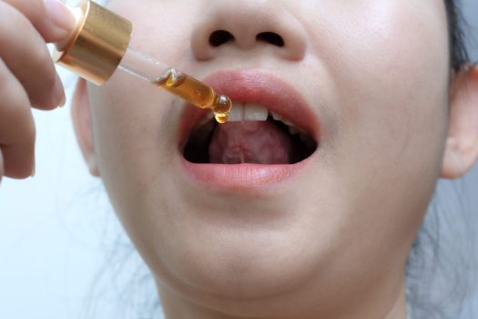 Woman holding a dropper sublingual Cannabis oil at white background